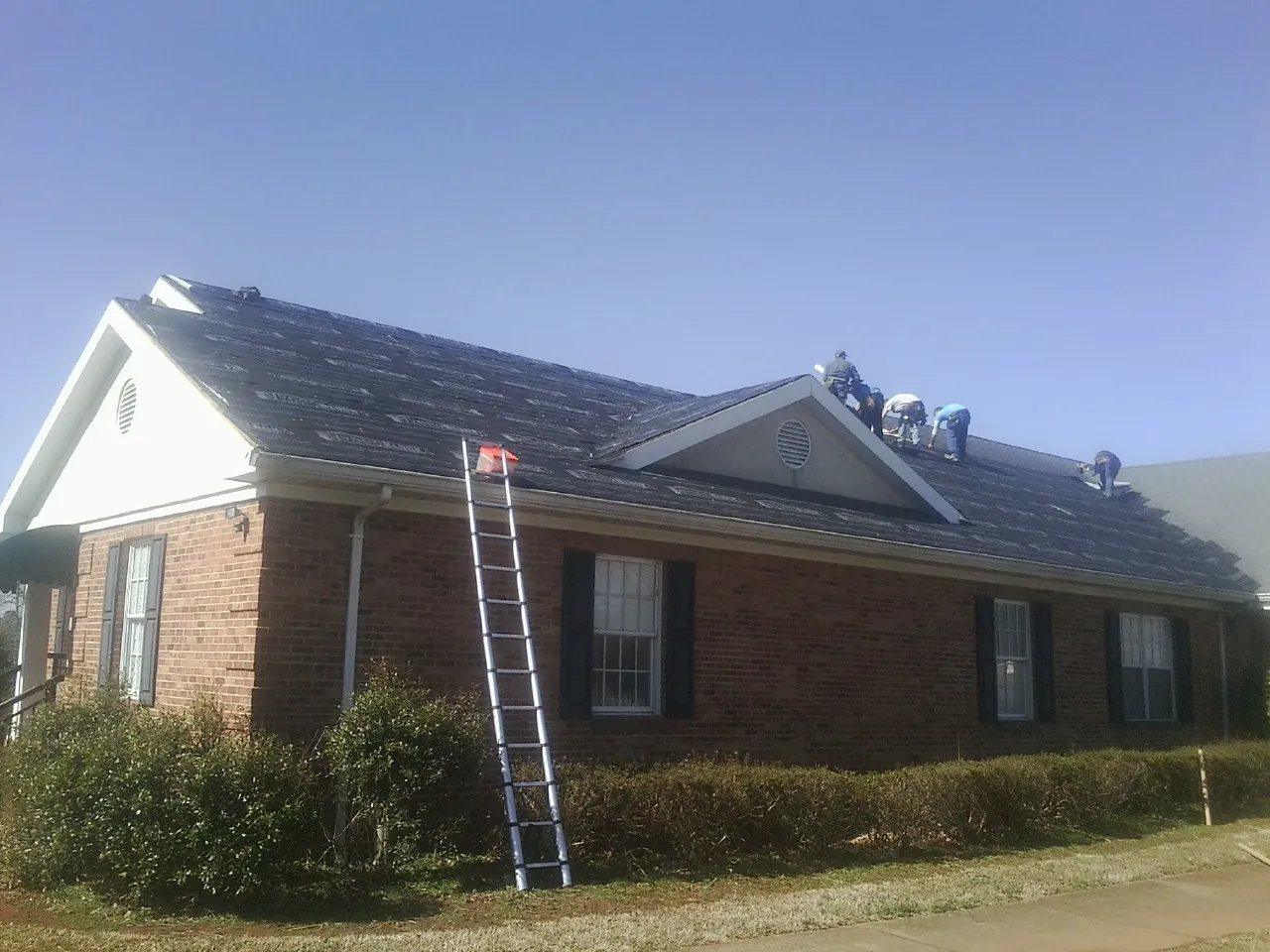 Crew tearing shingles off a brick ranch roof with a ladder set — Metal Roof Repair work by our crew in Lowell